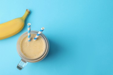 Photo of Mason jar of tasty banana smoothie with straws and fresh fruit on light blue background, flat lay. Space for text