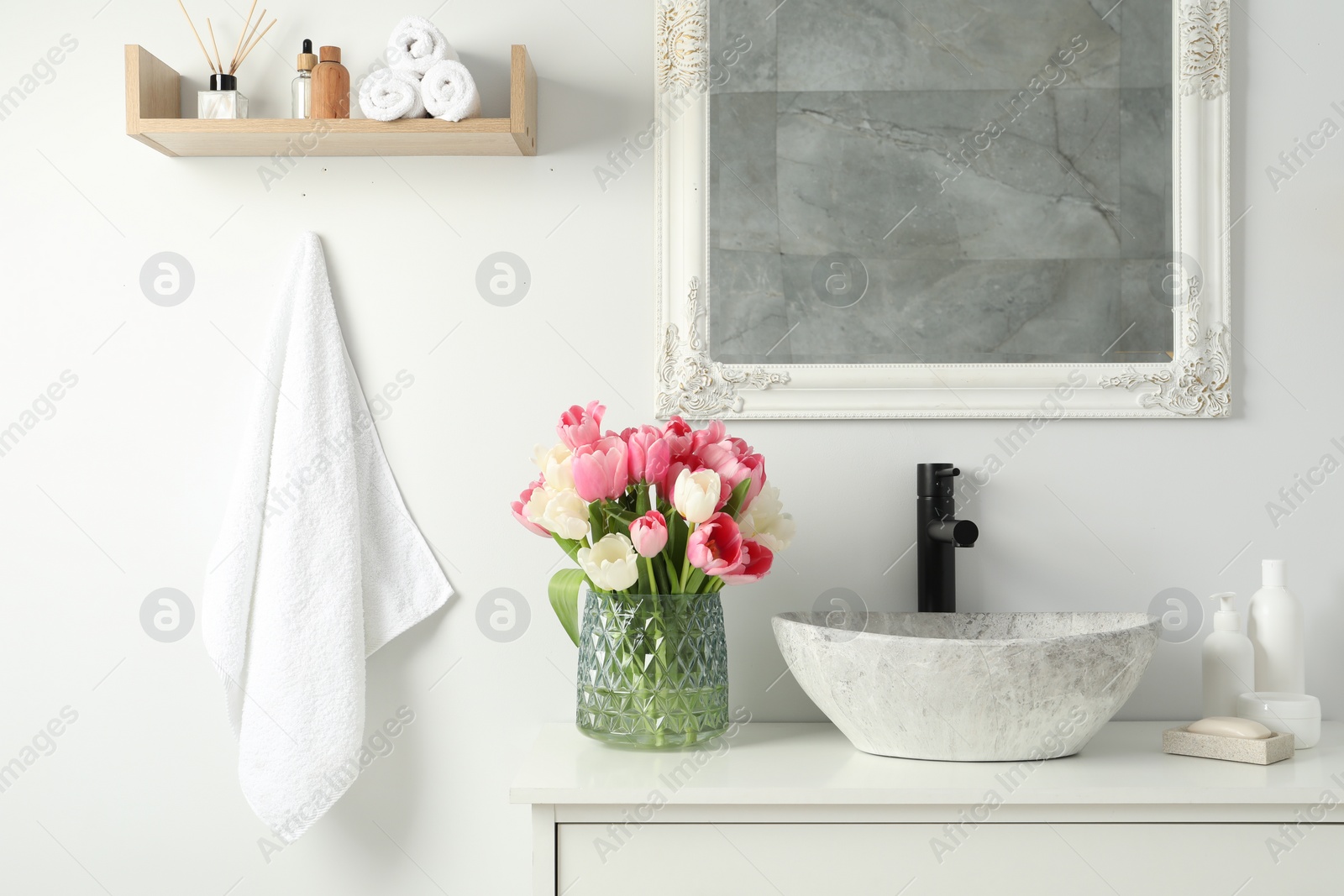 Photo of Vase with beautiful pink tulips and toiletries near sink in bathroom