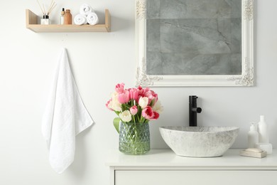 Vase with beautiful pink tulips and toiletries near sink in bathroom