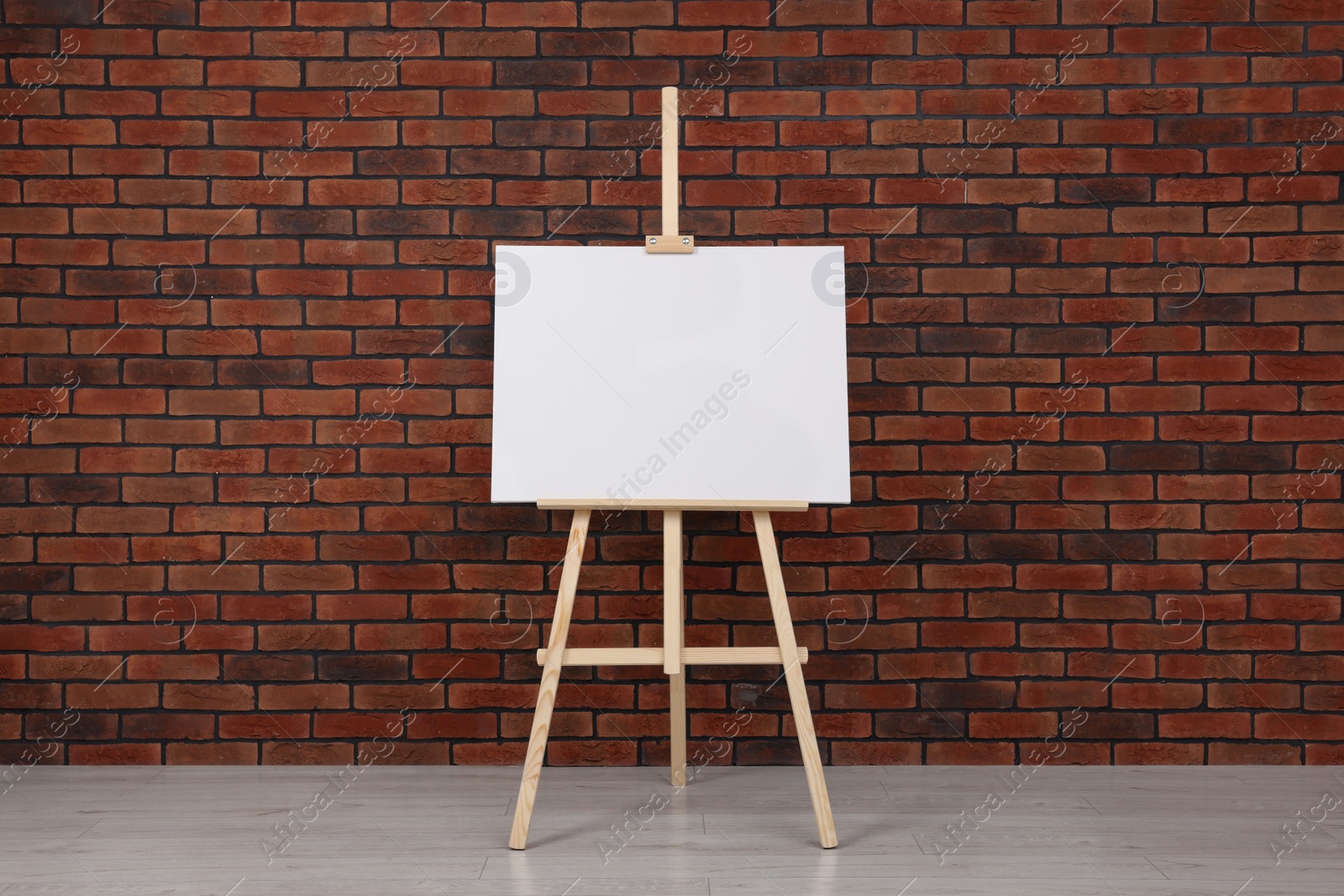 Photo of Wooden easel with blank canvas near brick wall indoors