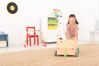 Cute little girl playing with wooden cart and toy at home, space for text