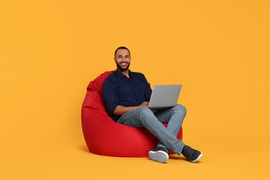 Smiling young man working with laptop on beanbag chair against yellow background