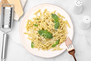 Plate of delicious trofie pasta with pesto sauce, cheese and basil leaves on white marble table, flat lay