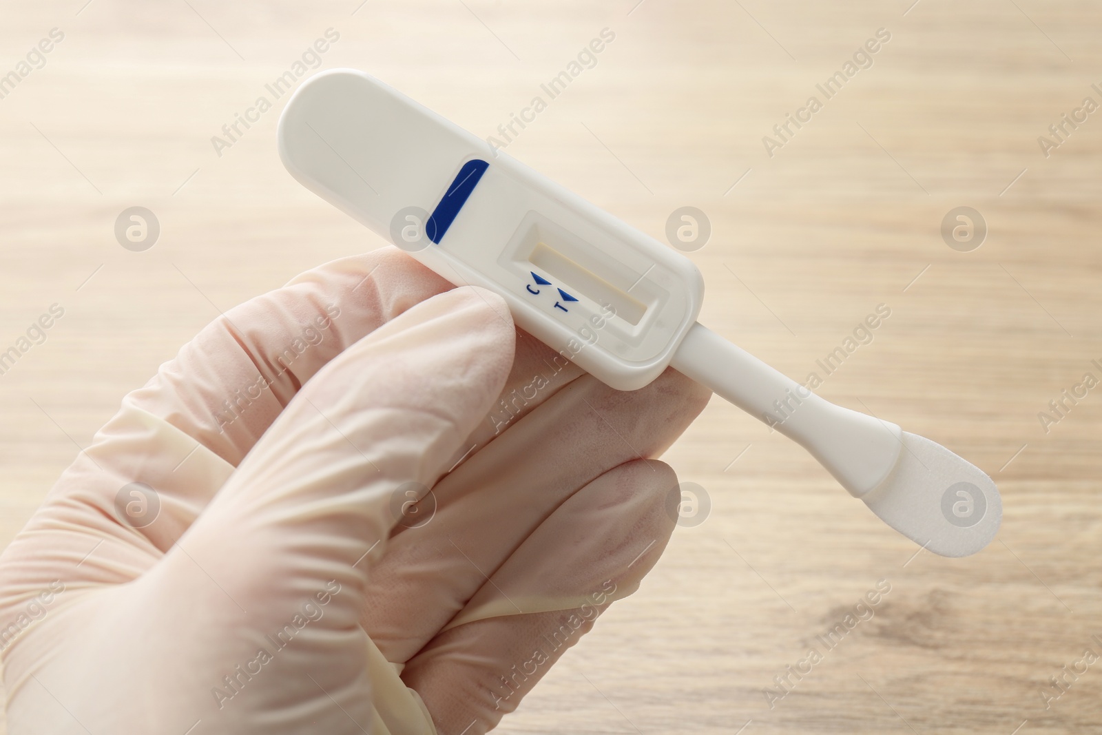 Photo of Woman holding disposable express test above wooden table, closeup