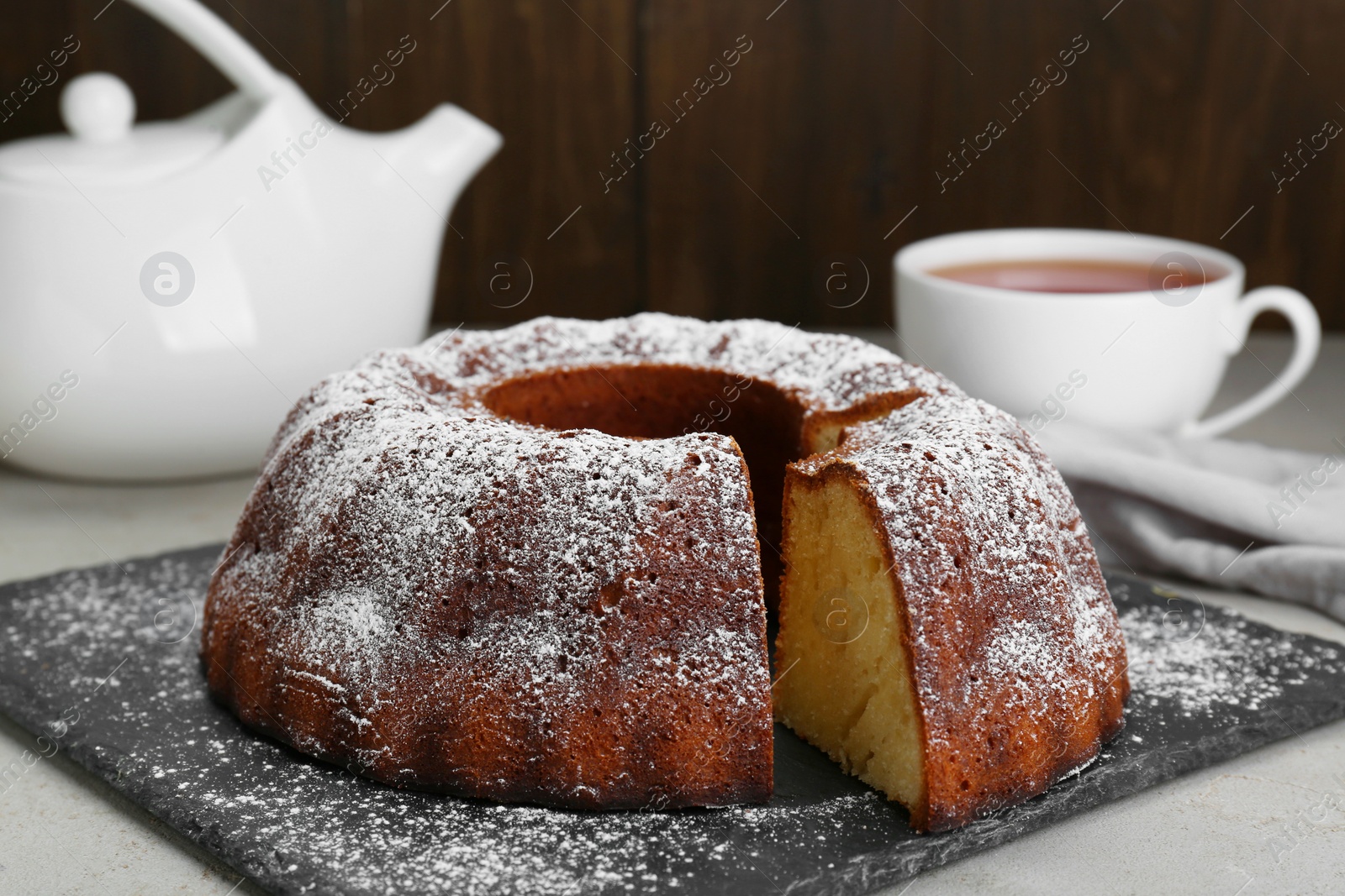 Photo of Homemade yogurt cake with powdered sugar on light grey table, closeup