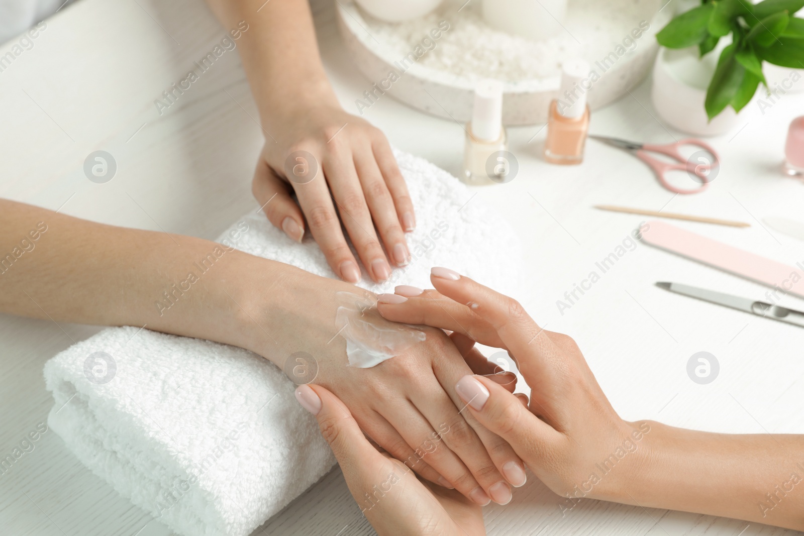 Photo of Cosmetologist applying cream on woman's hand at table in spa salon, closeup