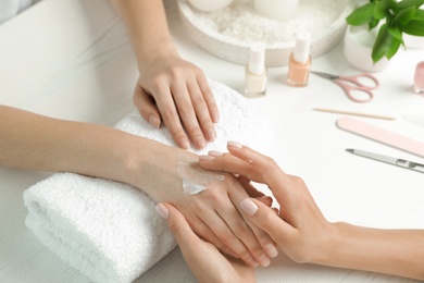 Photo of Cosmetologist applying cream on woman's hand at table in spa salon, closeup