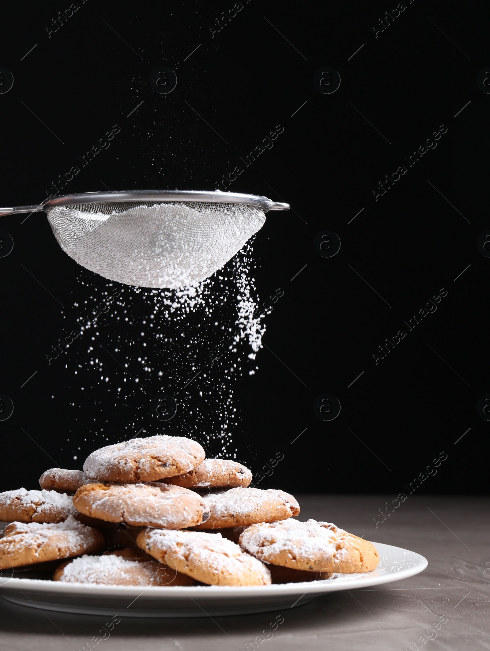 Photo of Woman with sieve sprinkling powdered sugar onto cookies at grey textured table, closeup