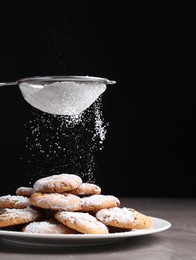 Woman with sieve sprinkling powdered sugar onto cookies at grey textured table, closeup