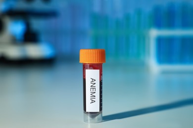 Test tube with blood sample and label Anemia on white table against blurred background