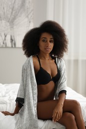 Photo of Beautiful woman in elegant black underwear and robe on bed indoors