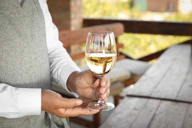 Photo of Waiter holding glass of white wine in outdoor cafe, closeup