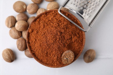 Nutmeg powder in bowl, seeds and grater on white table, flat lay