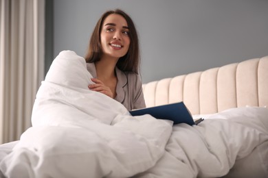 Photo of Beautiful young woman wrapped with soft blanket reading book on bed at home