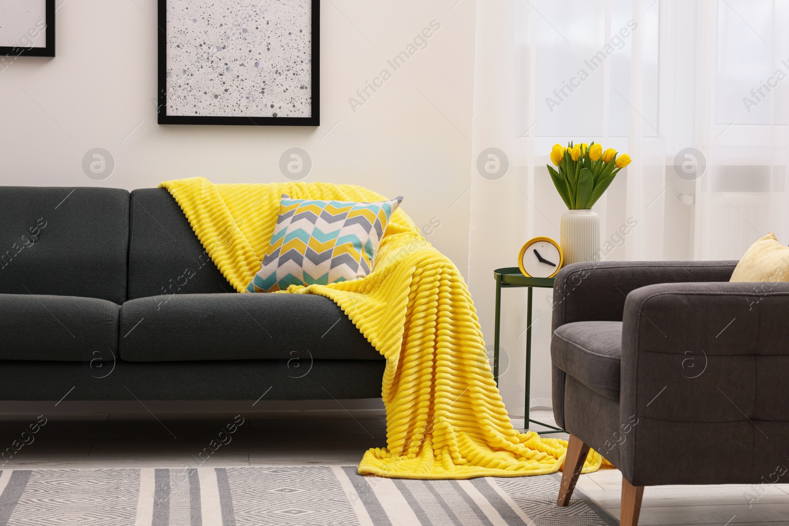 Photo of Spring atmosphere. Stylish living room interior with comfortable furniture and bouquet of beautiful yellow tulips