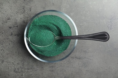 Photo of Bowl of spirulina algae powder with spoon on grey background, top view