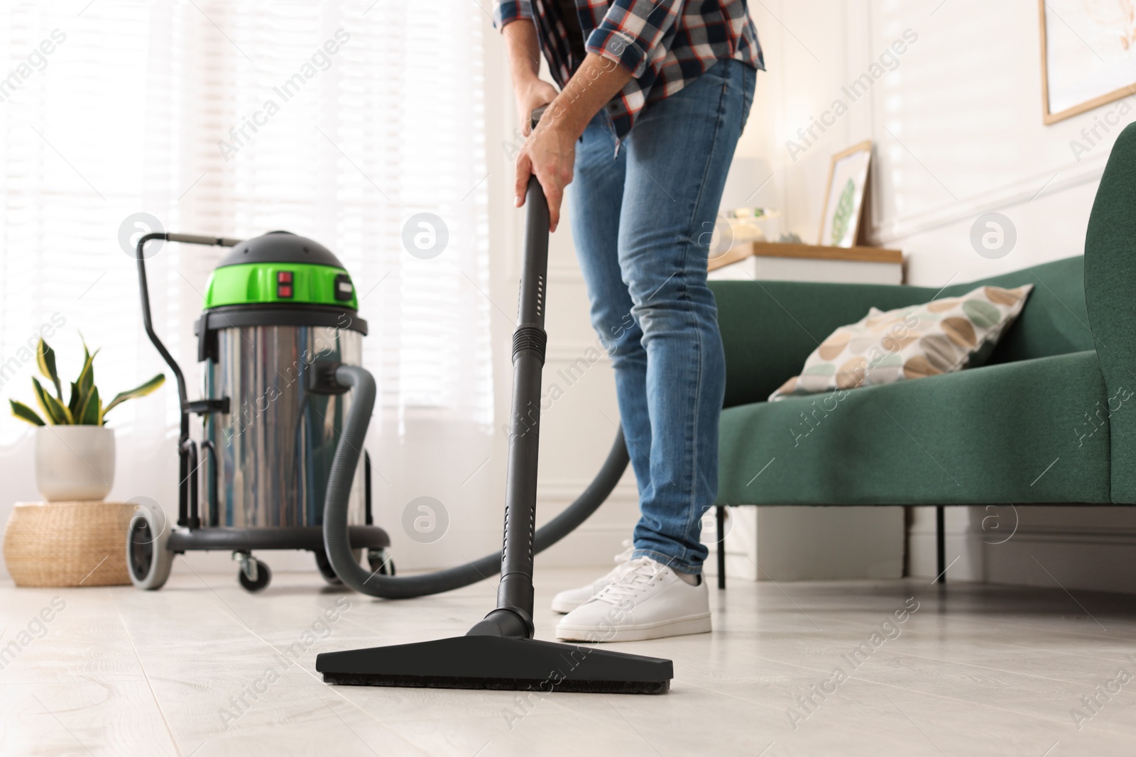 Photo of Woman vacuuming floor in living room, closeup