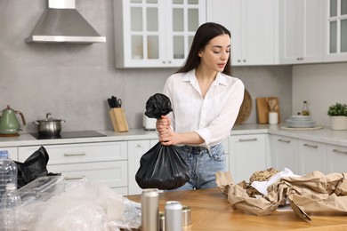 Garbage sorting. Woman with plastic bag at table in kitchen