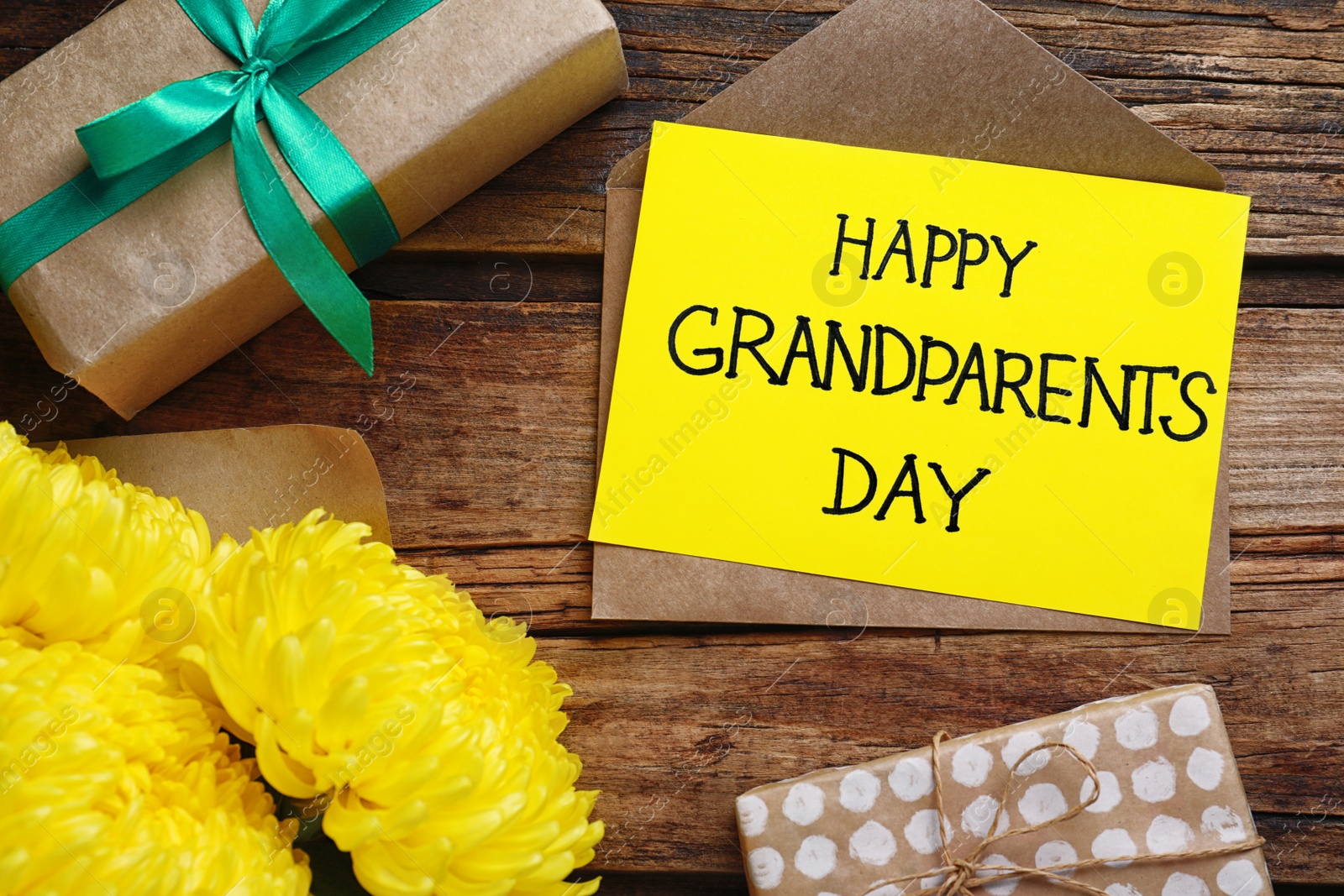 Photo of Beautiful flowers, gift boxes and card with phrase Happy Grandparents Day on wooden background, flat lay