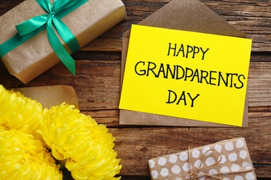 Beautiful flowers, gift boxes and card with phrase Happy Grandparents Day on wooden background, flat lay