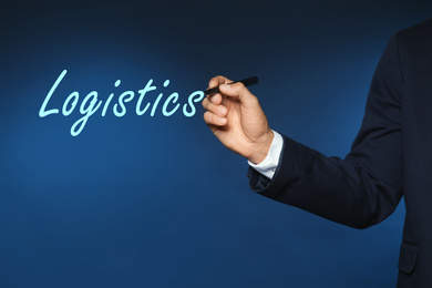 Businessman pointing at word LOGISTICS on virtual screen against blue background, closeup 