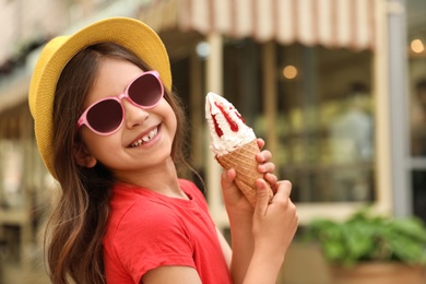 Cute little girl with delicious ice cream in park, space for text