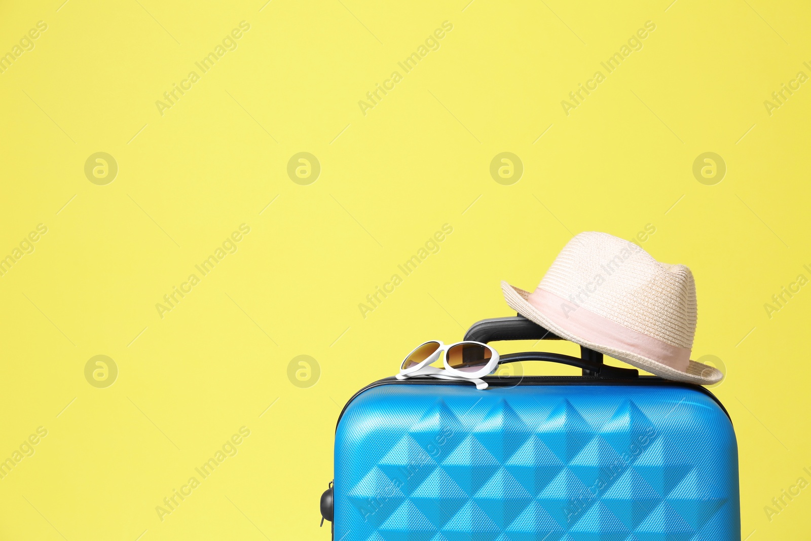Photo of Stylish blue suitcase with hat and sunglasses on yellow background. Space for text