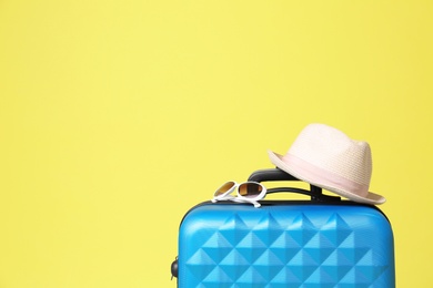 Stylish blue suitcase with hat and sunglasses on yellow background. Space for text