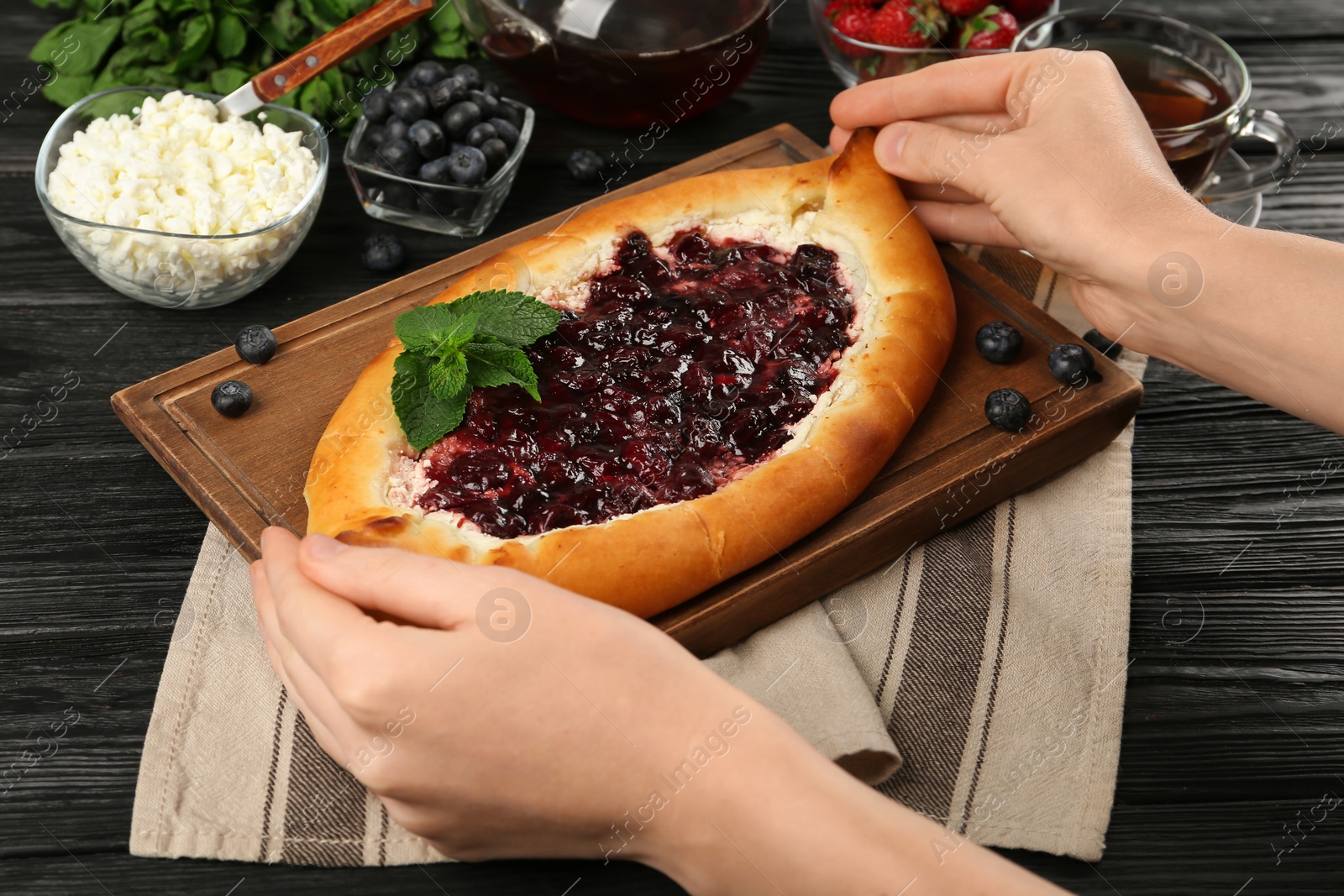 Photo of Woman eating delicious sweet cottage cheese pastry with cherry jam at wooden table, closeup