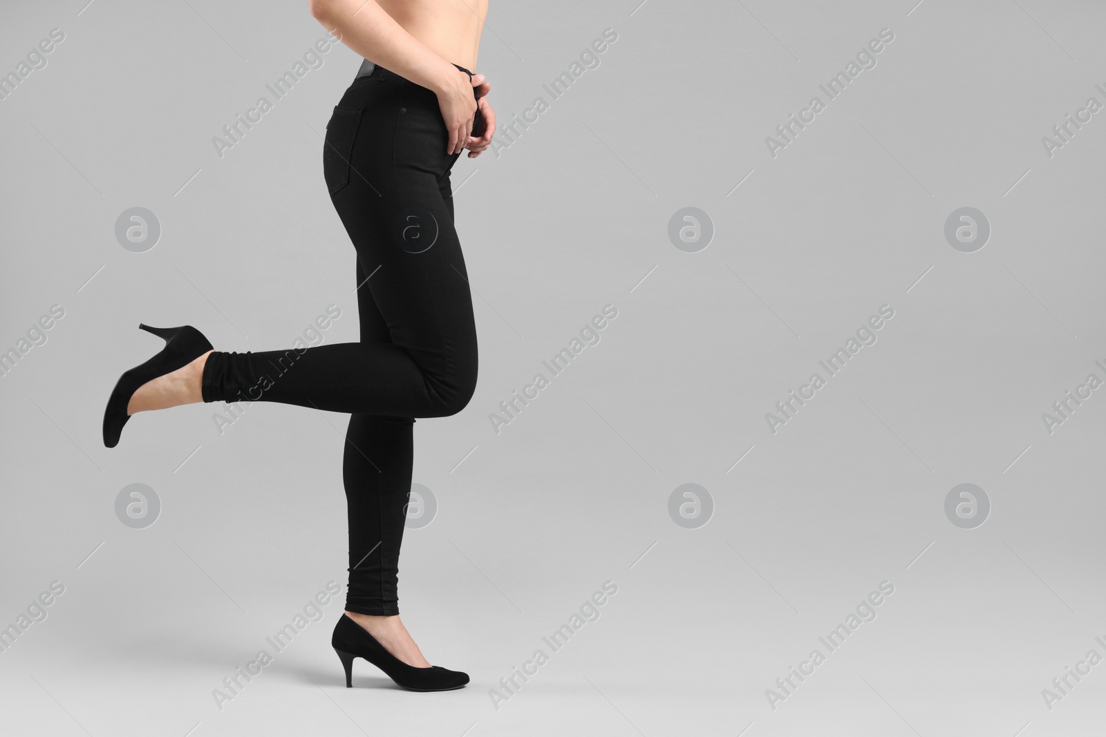 Photo of Woman wearing stylish black jeans and high heels shoes on light gray background, closeup. Space for text