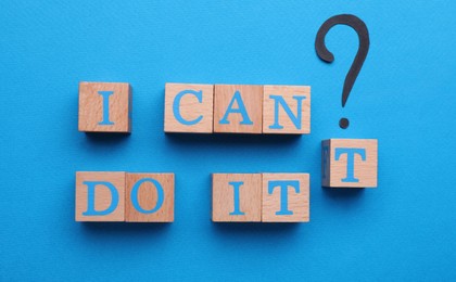 Photo of Motivation concept. Changing phrase from I Can't Do It into I Can Do It by removing wooden cube with letter T on light blue background, flat lay