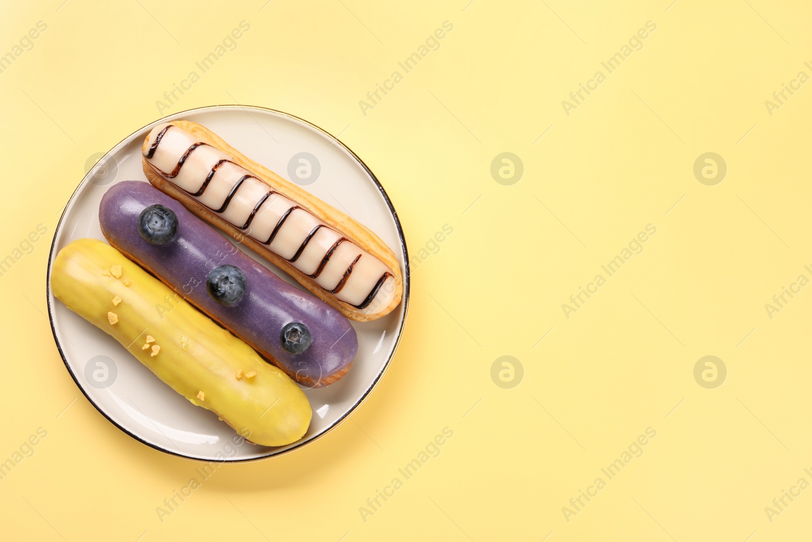 Photo of Delicious eclairs covered with glaze on yellow background, top view. Space for text