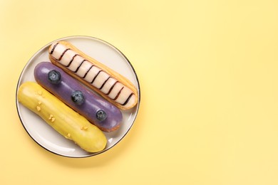 Photo of Delicious eclairs covered with glaze on yellow background, top view. Space for text