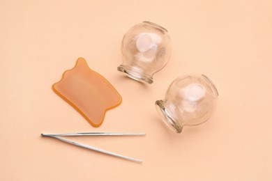 Photo of Glass cups, gua sha and tweezers on light coral background, flat lay. Cupping therapy