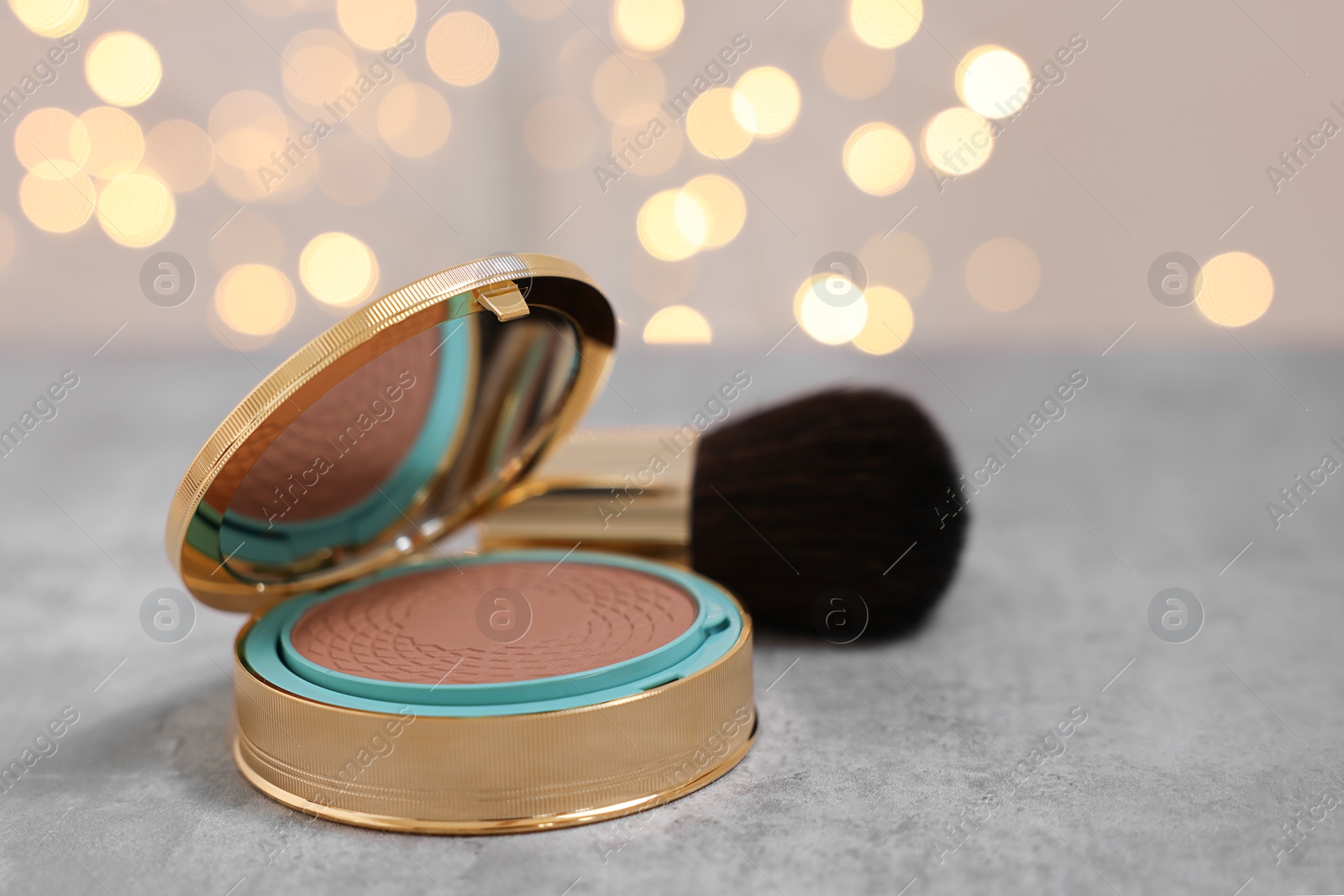 Photo of Face bronzer on grey textured table against blurred lights, closeup