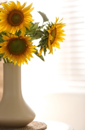 Vase with beautiful yellow sunflowers on table in room