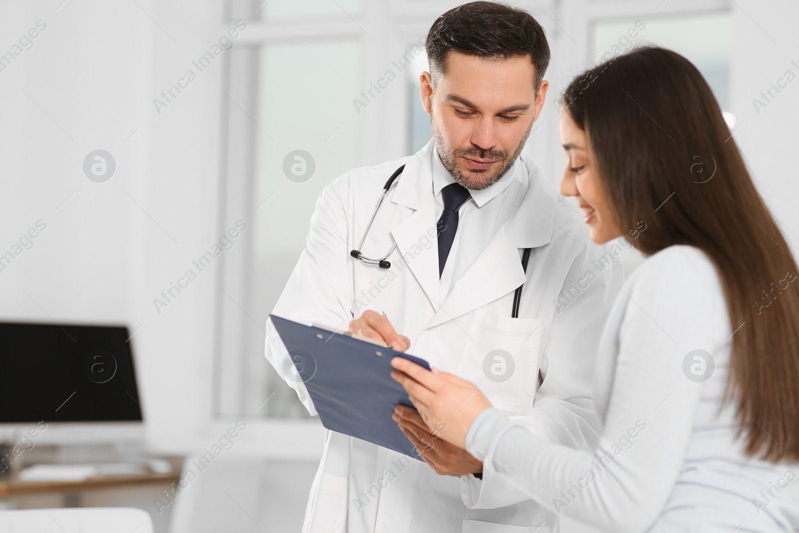 Photo of Doctor with clipboard consulting patient in clinic