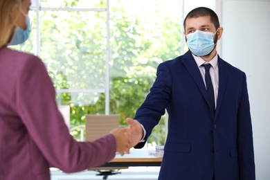 Photo of Man and woman in protective face masks shaking hands to say hello in office, closeup