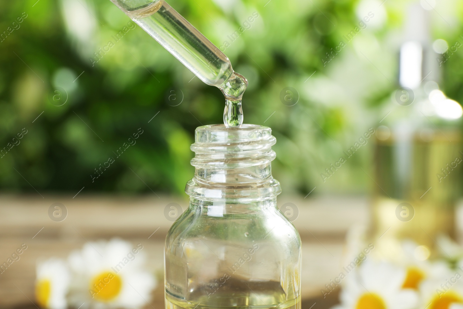 Photo of Dropping essential oil into bottle on blurred background, closeup