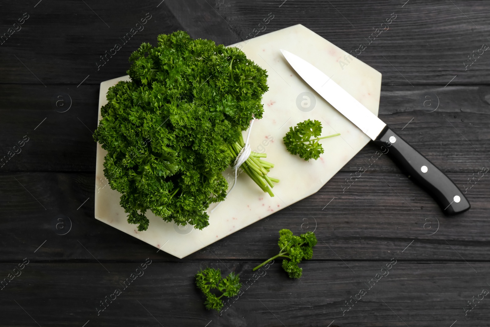 Photo of Fresh curly parsley, cutting board and knife on black wooden table, flat lay