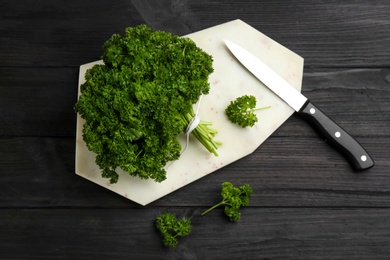 Fresh curly parsley, cutting board and knife on black wooden table, flat lay