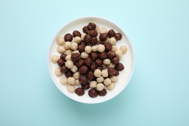 Photo of Breakfast cereal. Tasty corn balls with milk in bowl on light blue background, top view