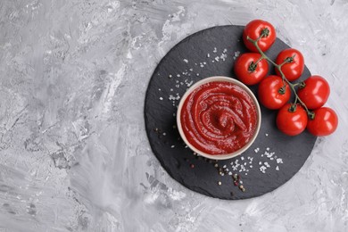 Photo of Organic ketchup in bowl, fresh tomatoes and spices on grey textured table, top view with space for text. Tomato sauce