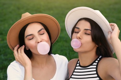 Beautiful women in hats blowing gums on green grass outdoors