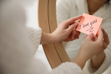 Woman with sticky note saying I Love You near mirror in bathroom, closeup. Romantic message