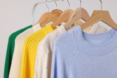 Rack with different warm sweaters on light background, closeup