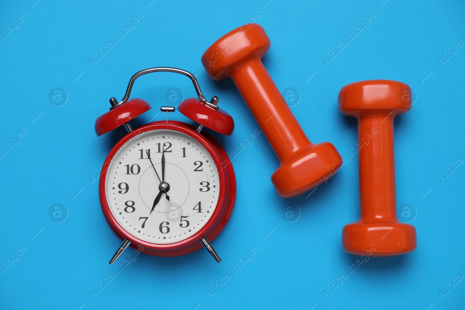 Photo of Alarm clock and dumbbells on light blue background, flat lay. Morning exercise