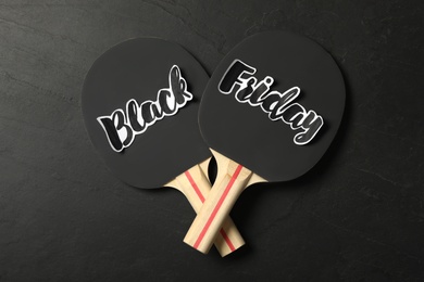 Photo of Table tennis rackets with phrase Black Friday on dark background, flat lay