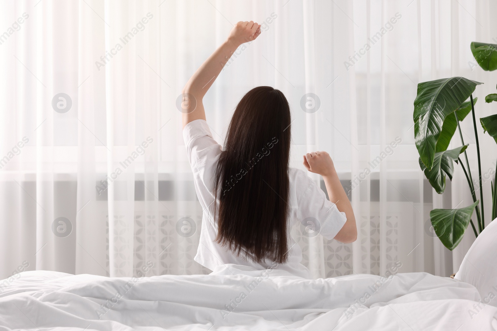 Photo of Woman stretching on bed at home, back view. Lazy morning