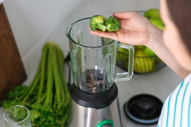 Photo of Woman adding broccoli into blender for smoothie in kitchen, closeup